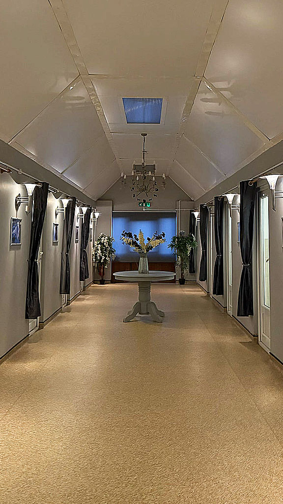 Grand Hallway, light and spacious, with a central table and vase of cream Delphiniums. Kennel doors are staggered for privacy on both sides and have dark grey satin curtains in front of glass and UPVC doors