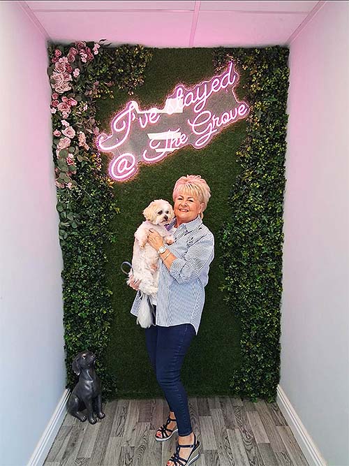 Bentley being held by his Mummy in front of our faux foliage and roses Selfie Wall with a pink and white neon sign saying 'I've stayed at The Grove'